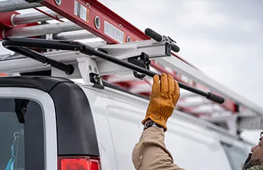 man unloading a ladder from an Adrian Steel ladder rack installed on the roof of a work van