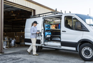 Woman walking past a work van with an open side door that shows the custom van upfit and shelving.